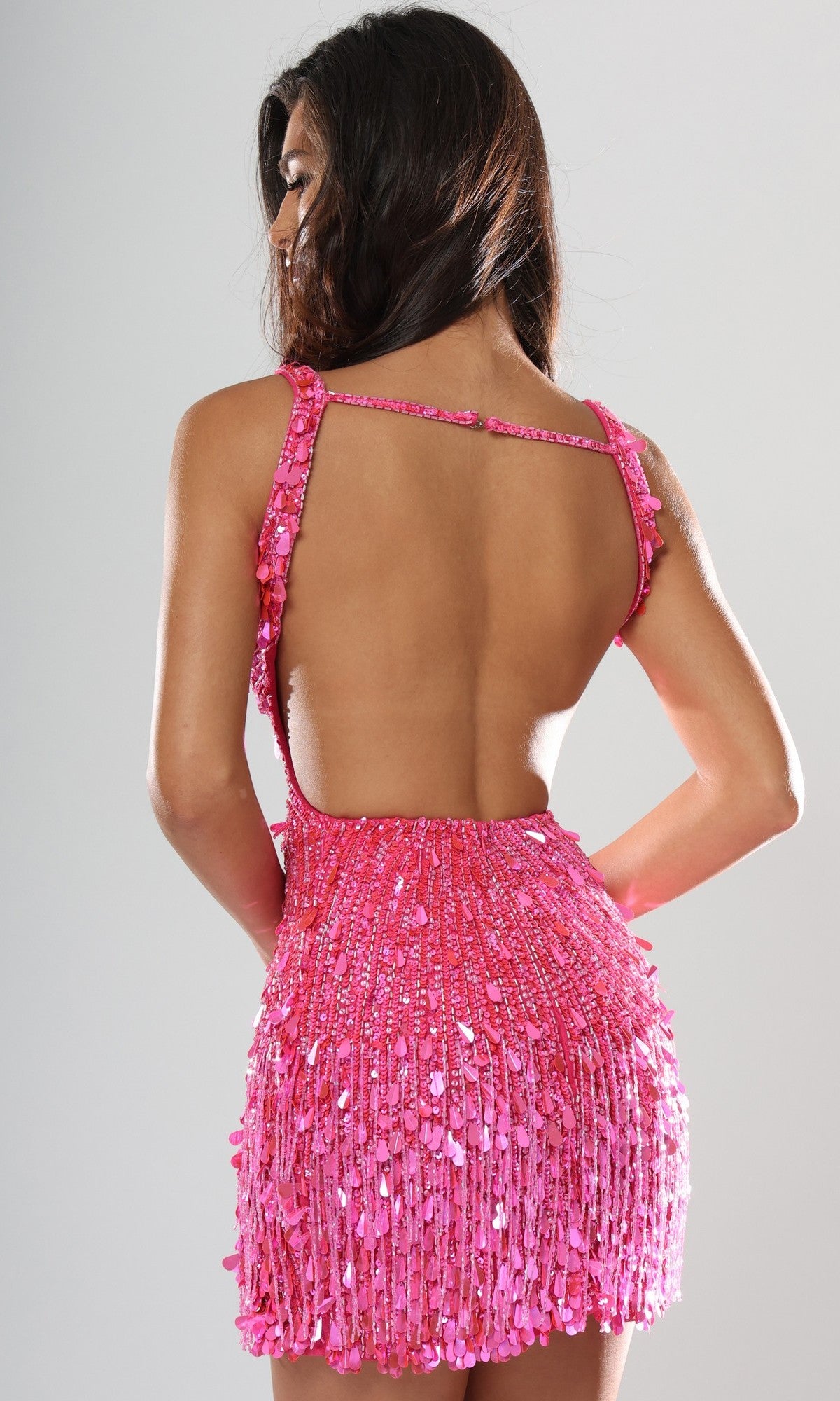 A woman faces away from the camera against a plain background, wearing the Jovani 51547 Short Homecoming Dress—a pink sequin mini dress with a low-cut open back.